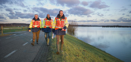 Afbeelding van drie toezichthouders lopend langs een dijk