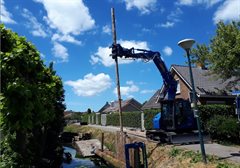 De ronde houten palen worden geplaatst langs de Lopikerwetering