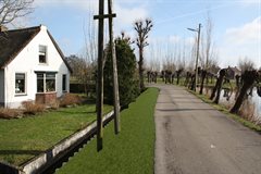 Impressiebeeld ter hoogte van Oost-Vlisterdijk 46. Het binnentalud is verbreed en het stabiliteitscherm is geplaatst. De palen steken 10cm boven het waterpeil uit.