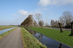 Impressiebeeld ter hoogte van het fietspad bij de Slangeweg na het afronden van de werkzaamheden. De bomen zijn gekapt, het binnentalud is verbreed en de palen van het stabiliteitscherm steken 15 cm boven het waterpeil uit.