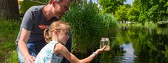 Man en meisje kijken naar een glazen pot gevuld met slootwater.