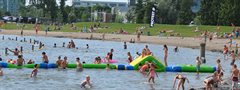 Volwassenen en kinderen zwemmen in het water. Er ligt ook een groot speelkussen op het water waar kinderen op spelen.