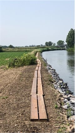 Het vlonderpad (houten planken die een pad vormen) bij de Gekanaliseerde Hollandsche IJssel. Rechts op de foto is de Gekanaliseerde Hollandsche IJssel te zien. Links op de afbeelding is een graslandschap te zien.