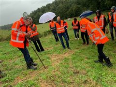 Verschillende Dijkwerkers in oranje veiligheidsjassen inspecteren de grond bij de dijk door met een stok in de grond te prikken.