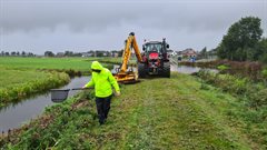 De ecoloog loopt met een schepnet voor de trekker met klepelmaaier uit tijdens het maaien