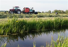 Sfeerbeeld landbouw veenweiden trekker in met balenpers in het land